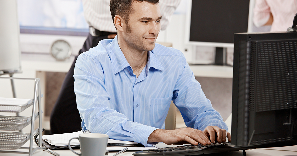 Casual businessman working in office, sitting at desk, typing on keyboard, looking at computer screen.