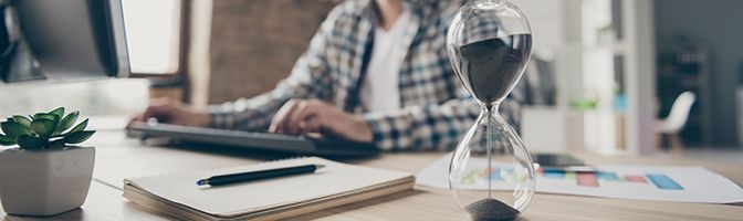 Blurred image of a person working at a computer with an hourglass in the forefront.