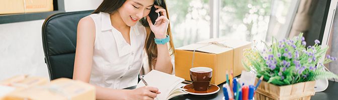 Business owner talking on a mobile phone while writing at their desk.