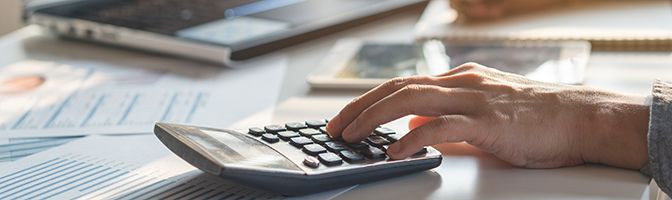 Close up of business professional using a calculator on top of documents.