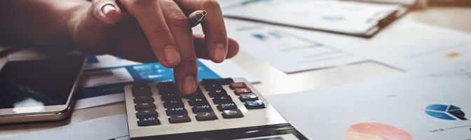 closeup of someone using a calculator on a table covered with reports