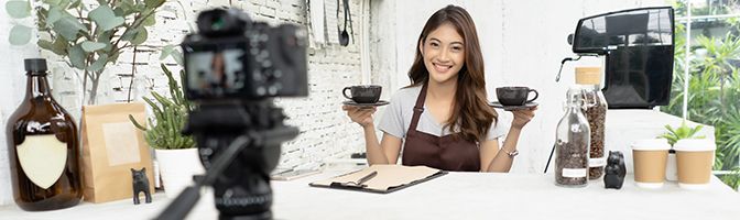 Business owner does a live stream in front of a camera in a coffee shop.