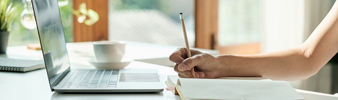 A person taking notes while viewing a laptop.