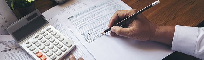 Close up photo of business person filling out a tax form with a calculator next to it.