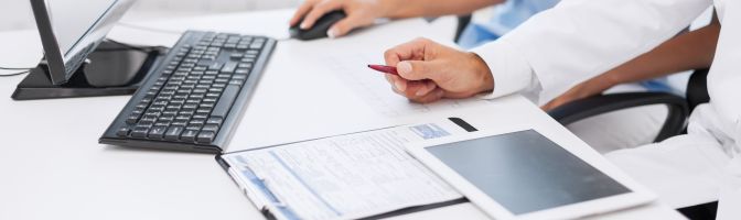 Doctor using tablet and computer to review charts