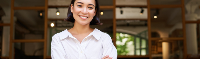 Smiling young female manager, cafe owner cross arms on chest, looking confident, standing in front of restaurant