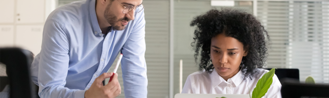 Business owner mentoring employee while they work on computer laptop