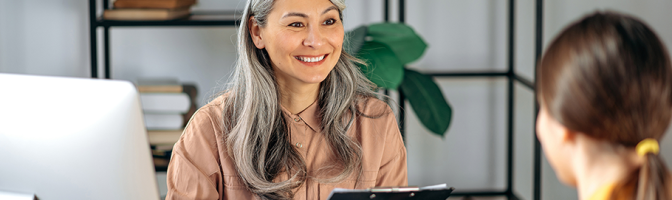 Mature businesswoman examines the resume of a female job seeker, sitting in office.