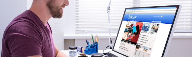 Man reading news on desktop computer at office desk