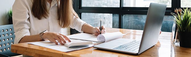 A business owner goes through reports at a desk with an opened laptop in front of her.