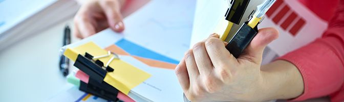 Closeup of a person's hand holding a large stack of paperwork.