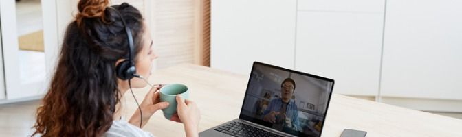 Woman holding a cup and wearing headphones while on a video conference call