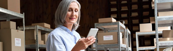 woman looking at phone and packing boxes in office storage shipping room