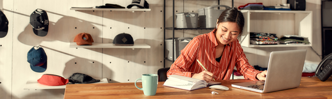 Female business owner making notes, receiving online orders while sitting in the office.