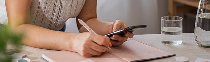 A business professional holds a smartphone while taking notes.