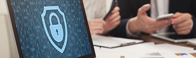 A laptop in the forefront shows a lock icon as a screensaver while two business professionals meet in thebackground.