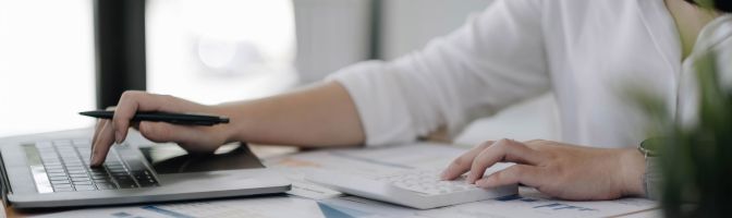 A person uses a calculator with one hand while typing on a laptop with the other.