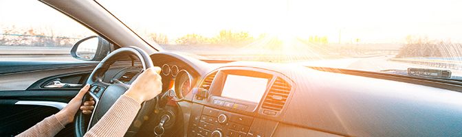 Side profile of a business person driving with both hands on a car's wheel.