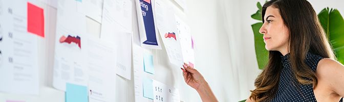 A small business owner reviews customer data pinned onto a large white board.