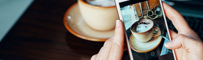 close up of someone using a cellphone with a cup of coffee in the background