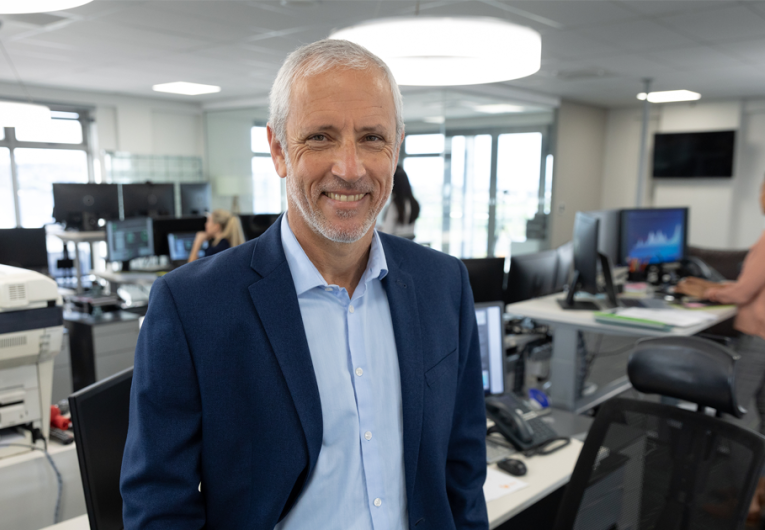   Save Download Preview Portrait of senior Caucasian businessman working in a modern office, standing and smiling to camera, colleagues in the background.