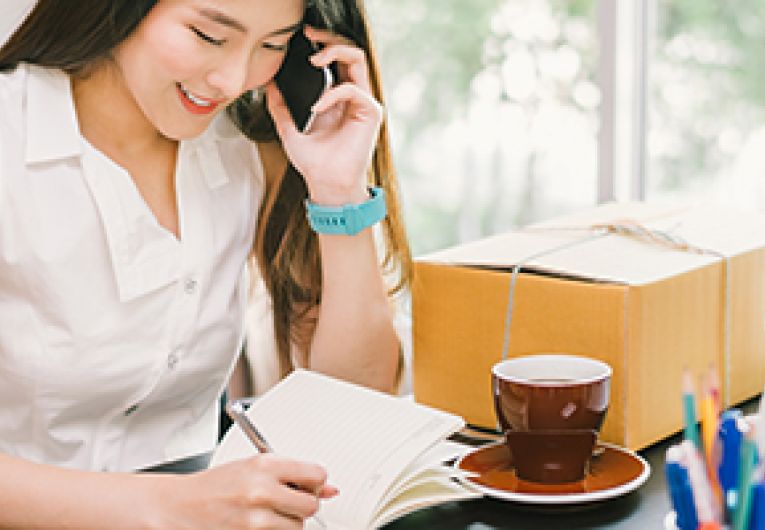 Business owner talking on a mobile phone while writing at their desk.