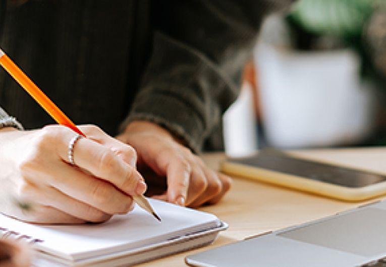 Close up of business owner writing on a notepad in front of a laptop.