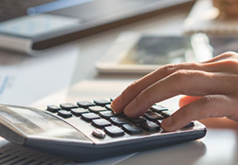 Close up of business professional using a calculator on top of documents.