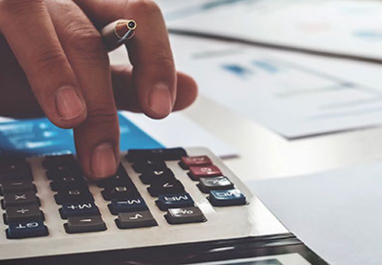 closeup of someone using a calculator on a table covered with reports