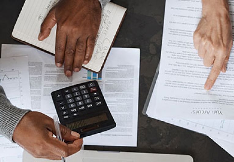 close up of people using a calculator over a paper strewn desk