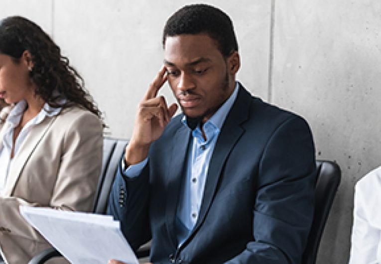 A group of potential applicants for a job sit in a row of seats while they read documents.