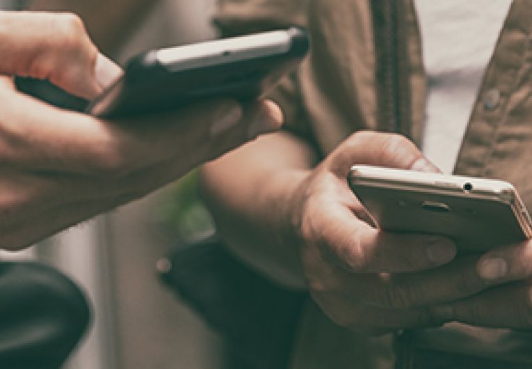 Closeup of the hands of two people doing a search through their mobile devices.