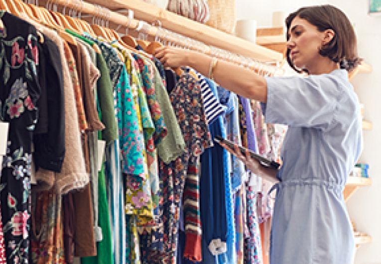 Small business owner checks back-to-school clothing inventory in her store with tablet device. 