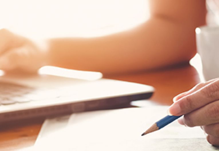 Closeup on a person with one hand on a laptop keyboard while holding a pencil in the other hand.