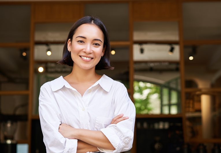 Smiling young female manager, cafe owner cross arms on chest, looking confident, standing in front of restaurant