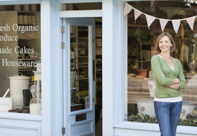 Woman working in local shop standing in front of store front 