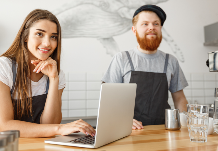 Cheerful baristas working on their laptop in modern coffee shop.