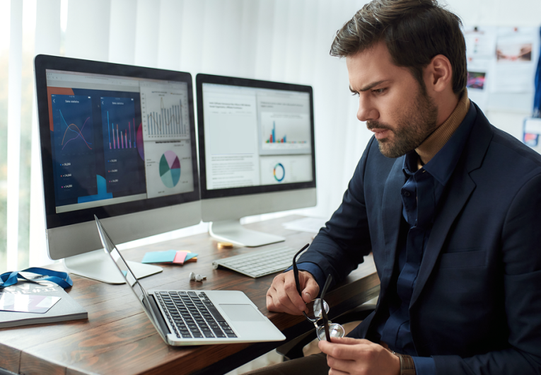 Young focused businessman or financial analyst sitting at his workplace in the office and working on laptop. 