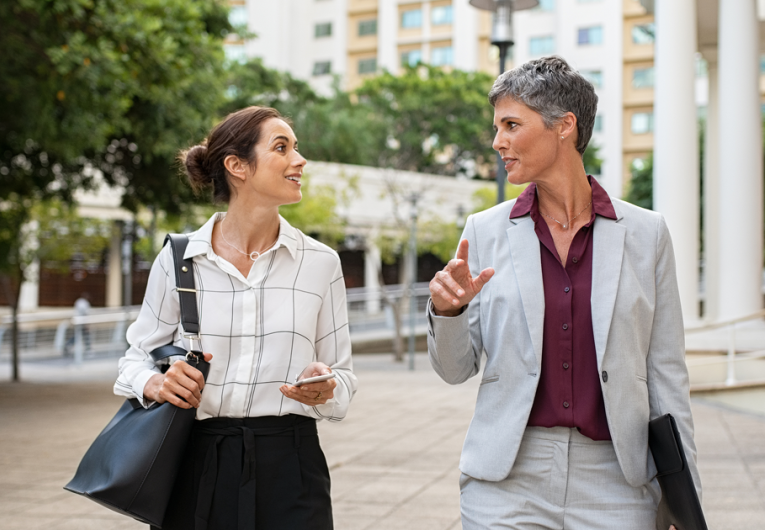 Two business women in conversation walking on city street.