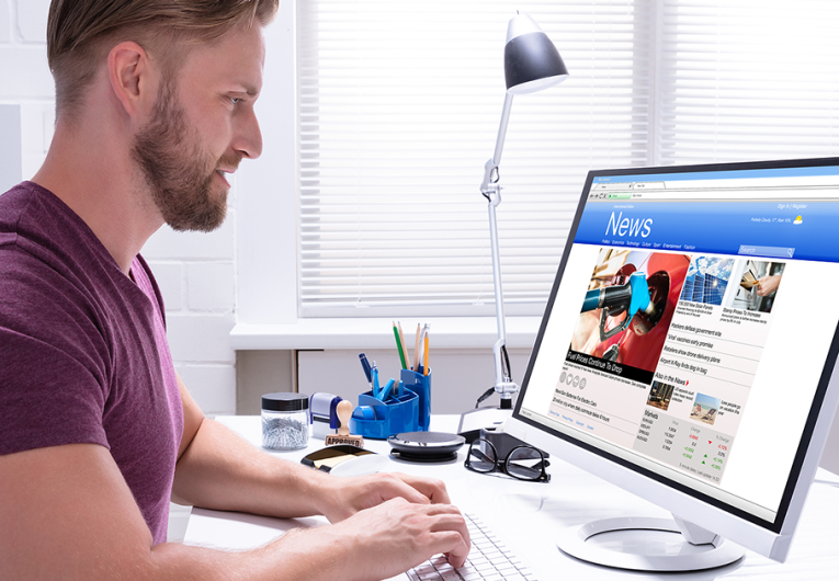 Man reading news on desktop computer at office desk