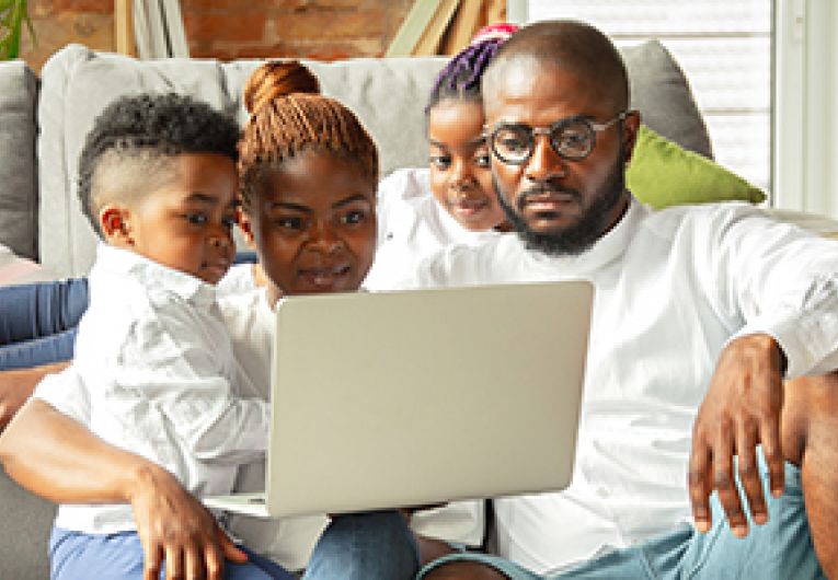 Family of four relax in their living room watching a movie through a laptop.