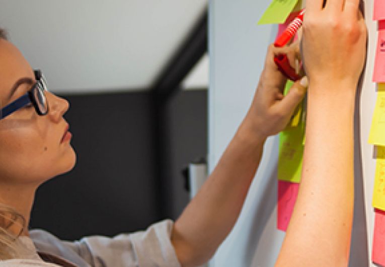 Business owner writing on sticky notes placed on a wall.