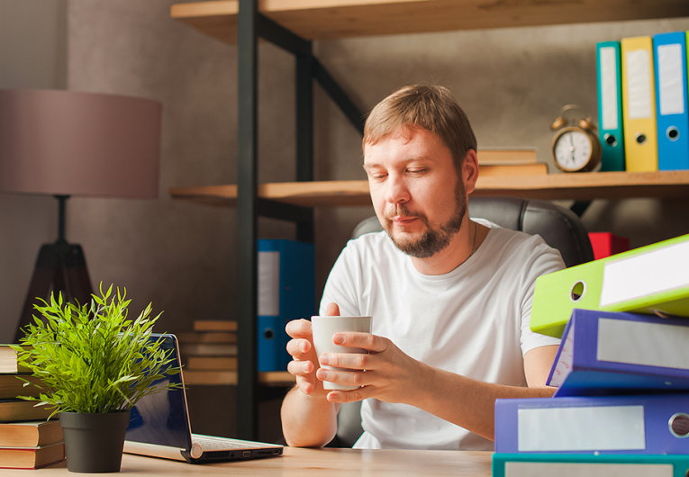 A man in the office behind a stack of folders and a laptop.