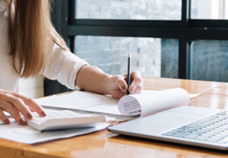 A business owner goes through reports at a desk with an opened laptop in front of her.