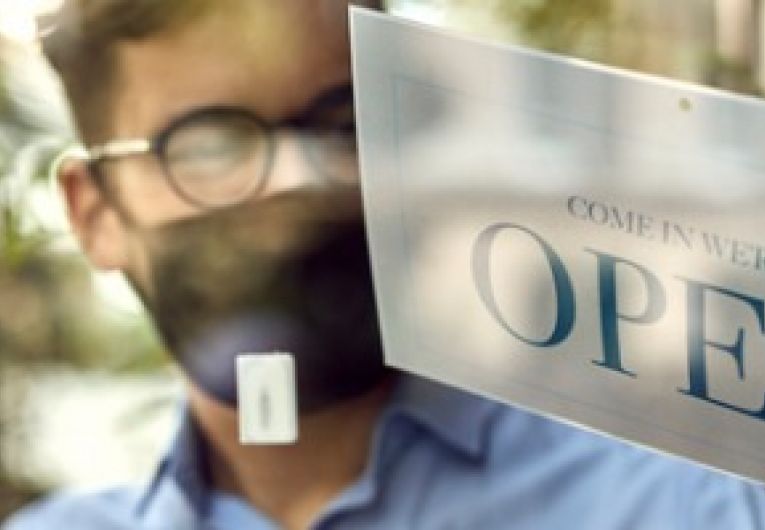 Business owner wearing a mask and gloves displays the open sign