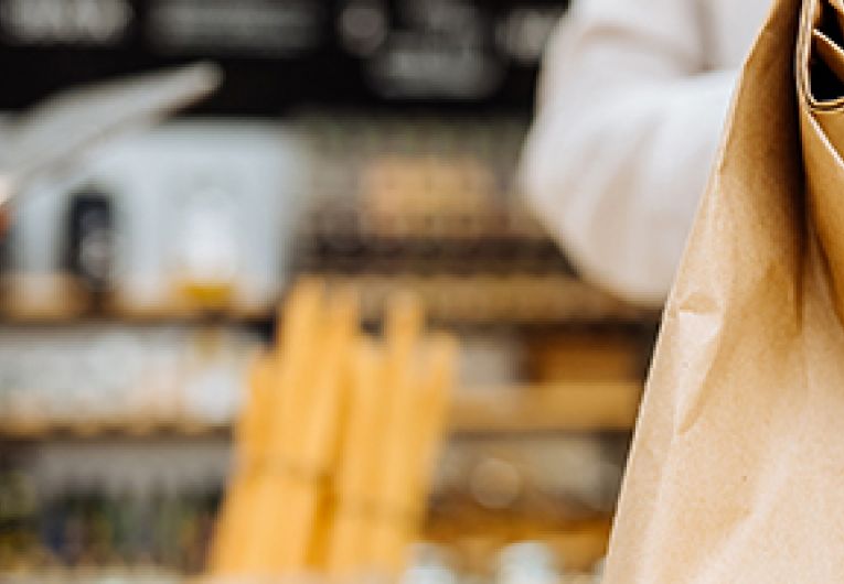 Small business employee use a tablet in the background while another employee holds a paper bag.