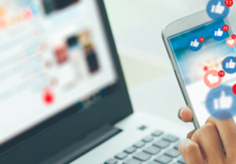 A person holds a smartphone that has social media icons floating through the screen.