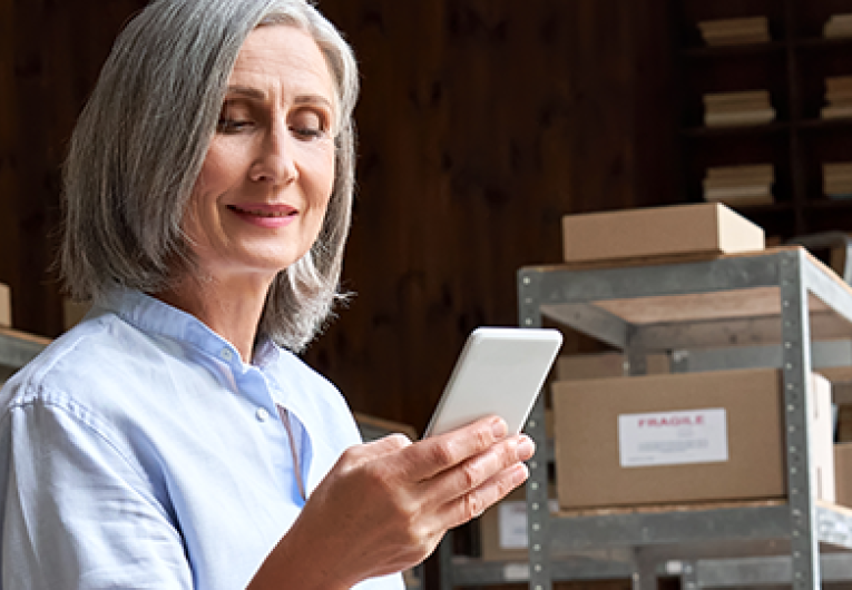 woman looking at phone and packing boxes in office storage shipping room