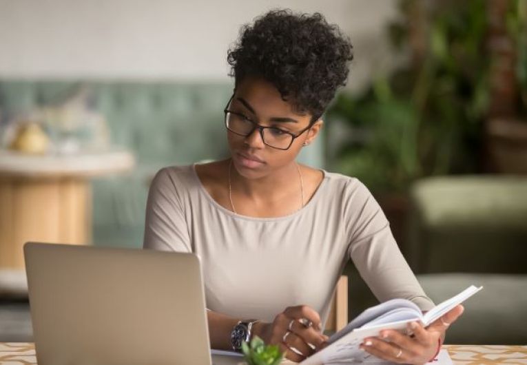 Woman taking notes while viewing a laptop