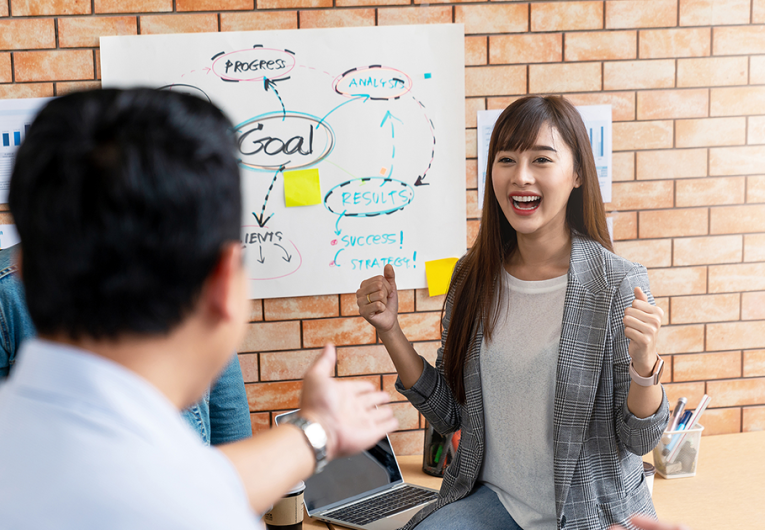 Businesswoman expressing happiness while she meets with team of employees to discuss goals